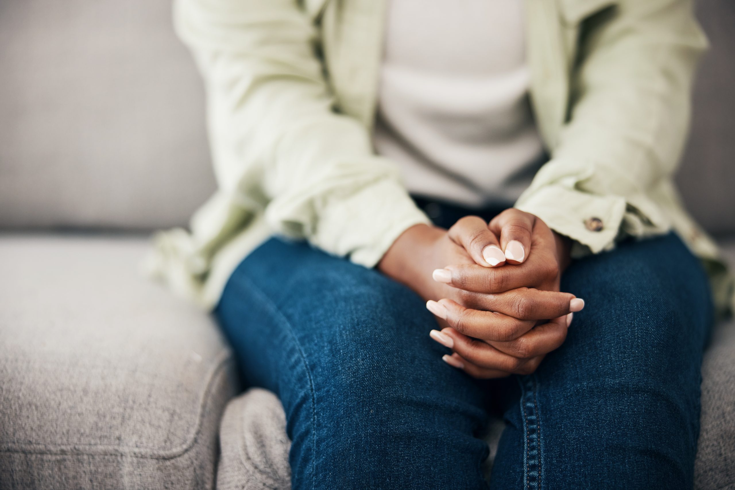 Anxiety, hands and woman on a sofa with stress, fear or worry for mental health or domestic abuse in her home. Psychology, zoom and female with depression, bipolar or scared of gender based violence.